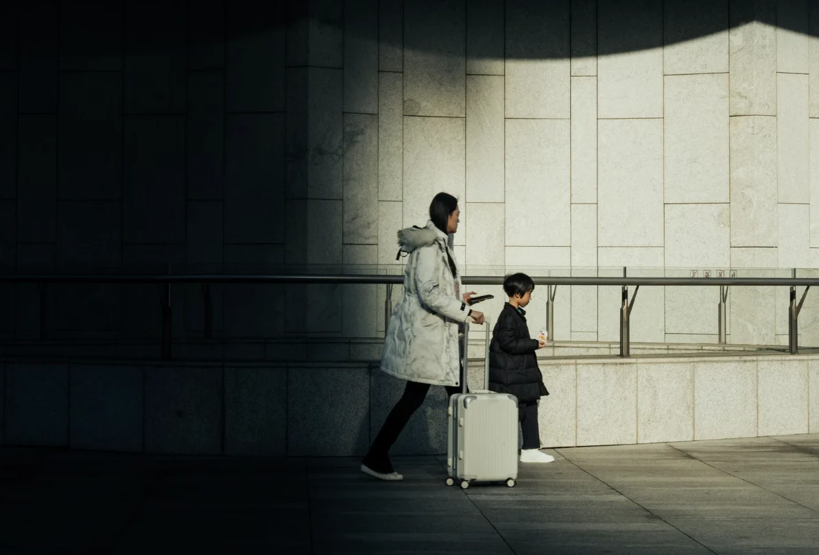 A parent and child walking through an airport with luggage.
