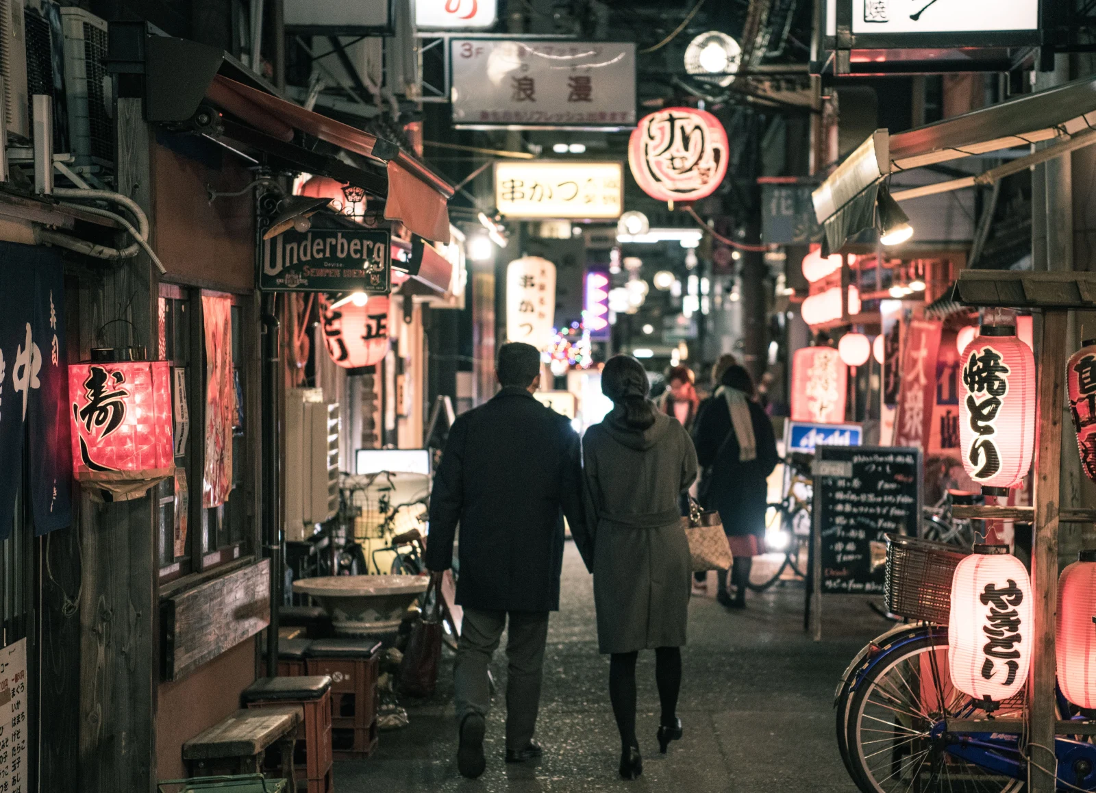 A couple walking through a lantern-lit street in Japan, seen from behind.