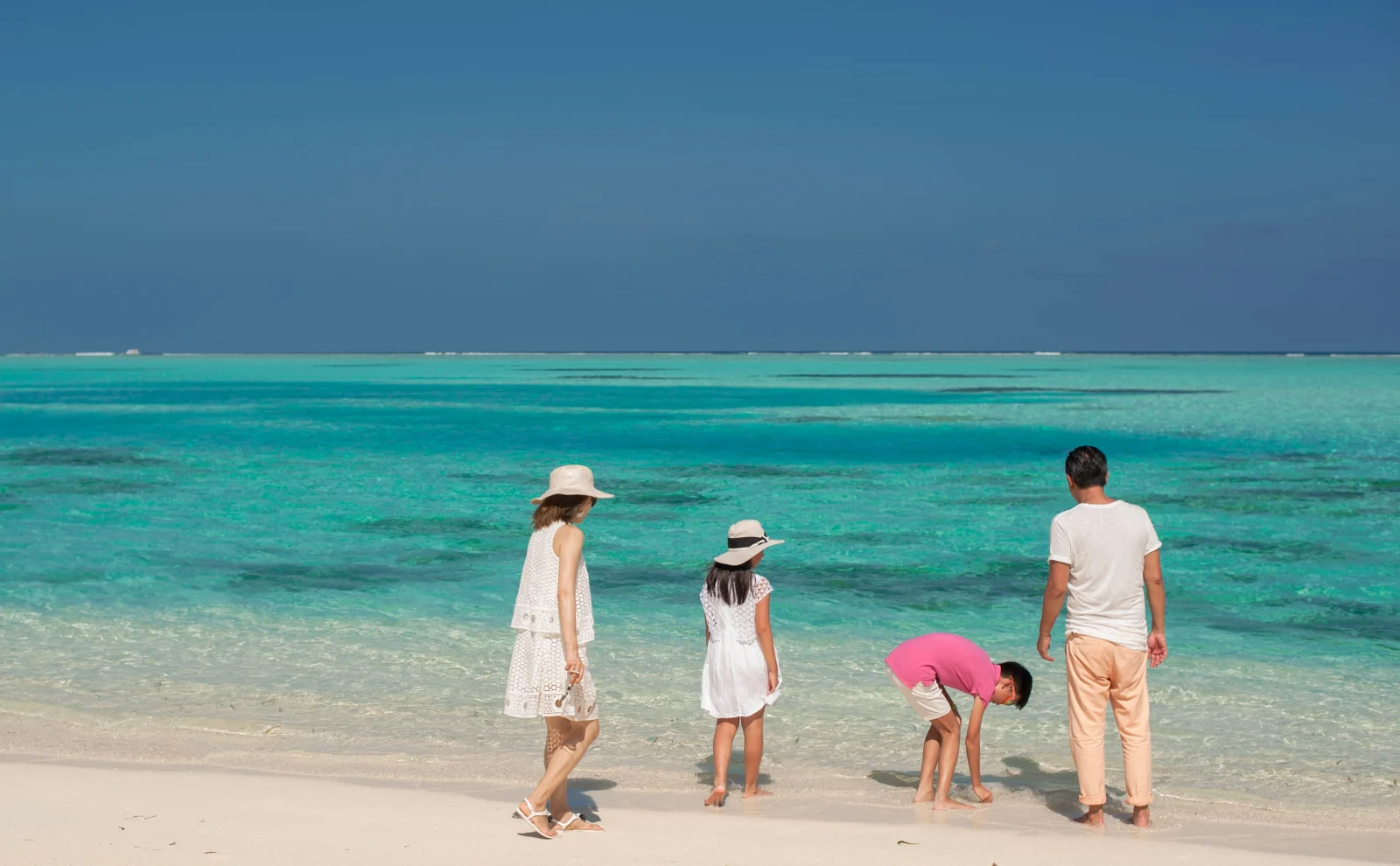 A family with two children standing at the ocean, seen from behind.